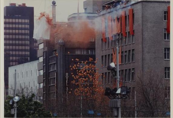 Met oranje versierde gebouwen, oranje ballonnen en rook.