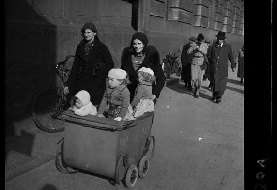 Vrouw loopt met kinderwagen en kinderen langs het postkantoor aan de Coolsingel.