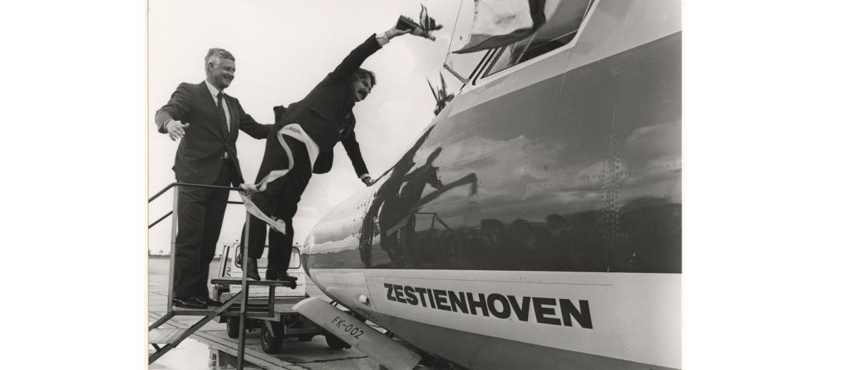 Burgemeester Van der Louw doopt met een fles champagne een vliegtuig.